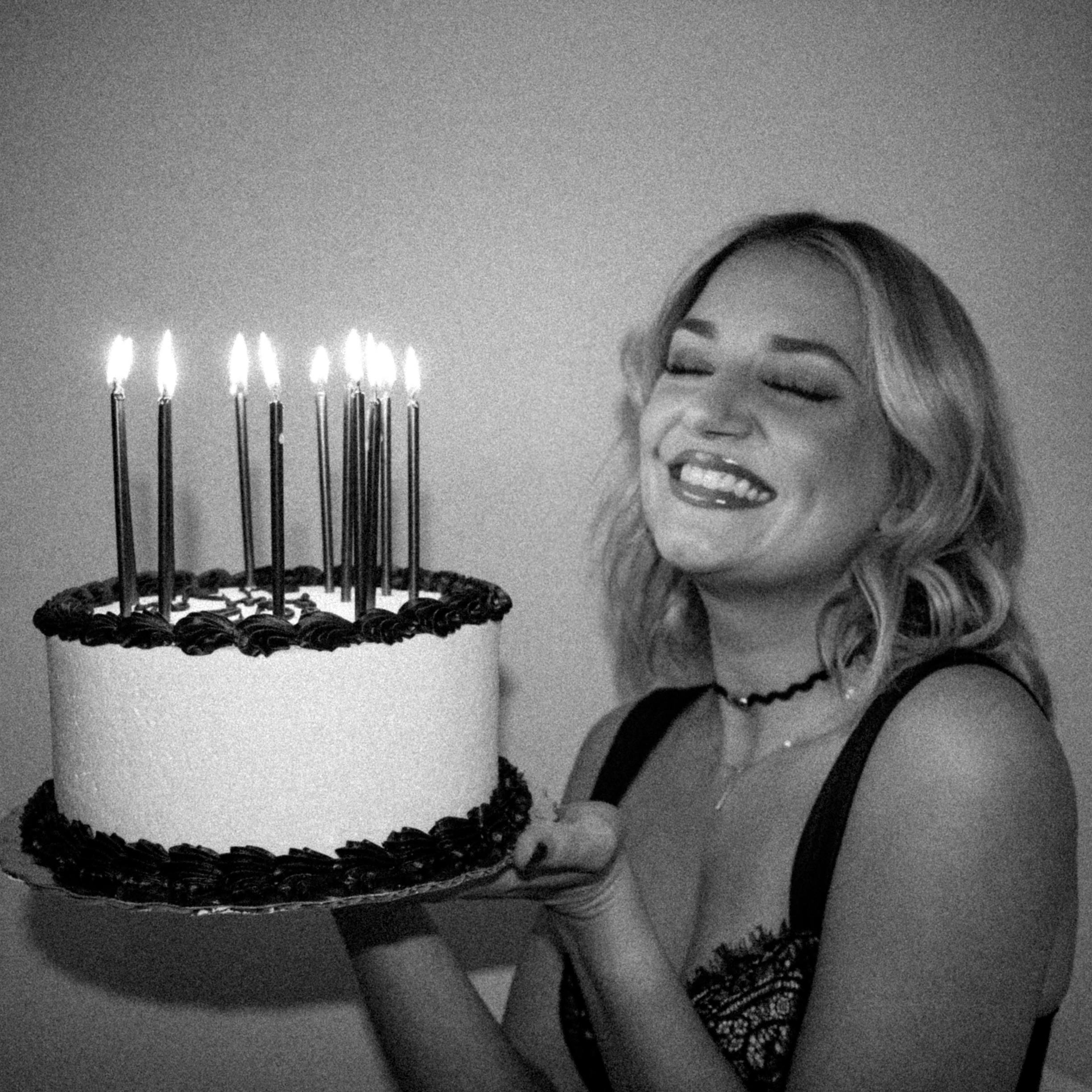 Woman joyfully holding a lit birthday cake indoors.