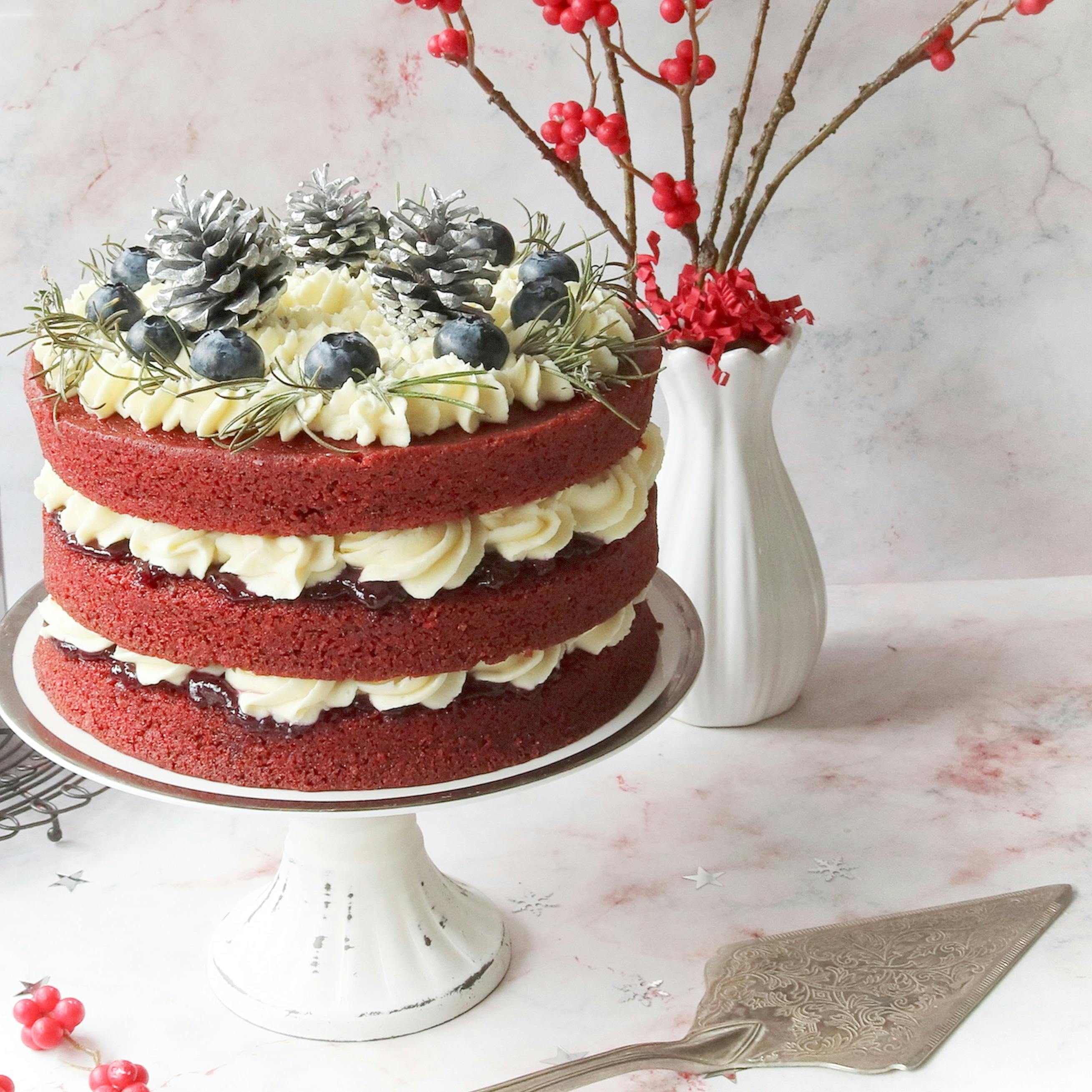 Elegant red velvet cake with blueberries, cream, and decorative pine cones.